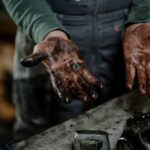 Close-up of a mechanic's dirty hands in a garage workspace with grease and spare parts.