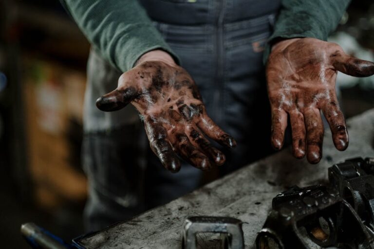 Close-up of a mechanic's dirty hands in a garage workspace with grease and spare parts.