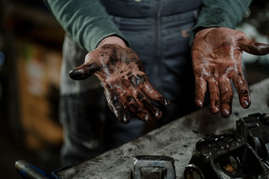 Close-up of a mechanic's dirty hands in a garage workspace with grease and spare parts.