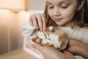 A smiling child appreciates a handcrafted soap with dried flowers in a warm, cozy setting.