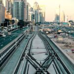 A dynamic view of Dubai's cityscape with bustling traffic and rail tracks in the foreground.