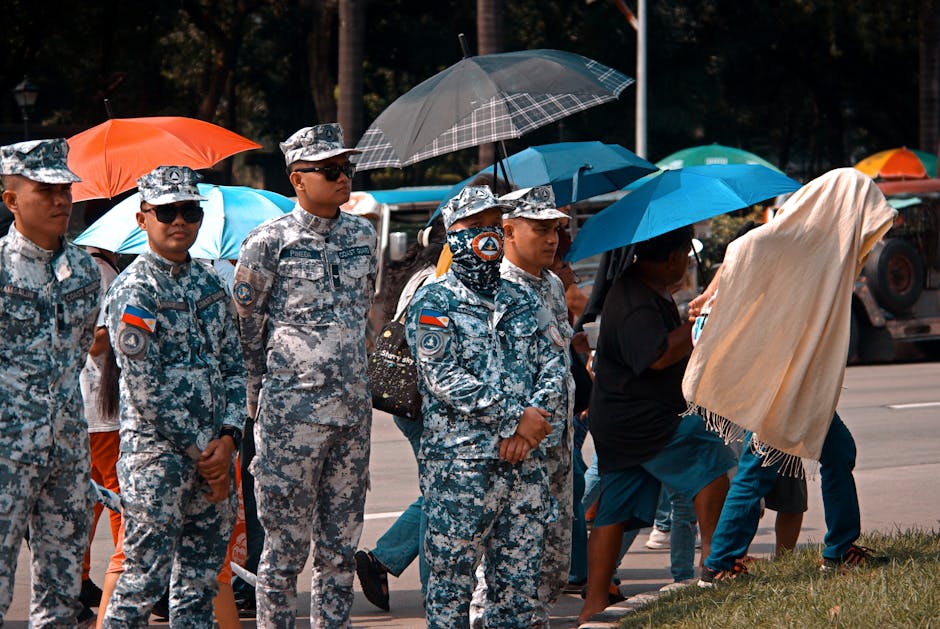 Military personnel stand with umbrellas in a street, showing resilience during a rainy event.
