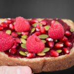 Close-up of a delicious multigrain toast topped with raspberries, pomegranate seeds, and pumpkin seeds.