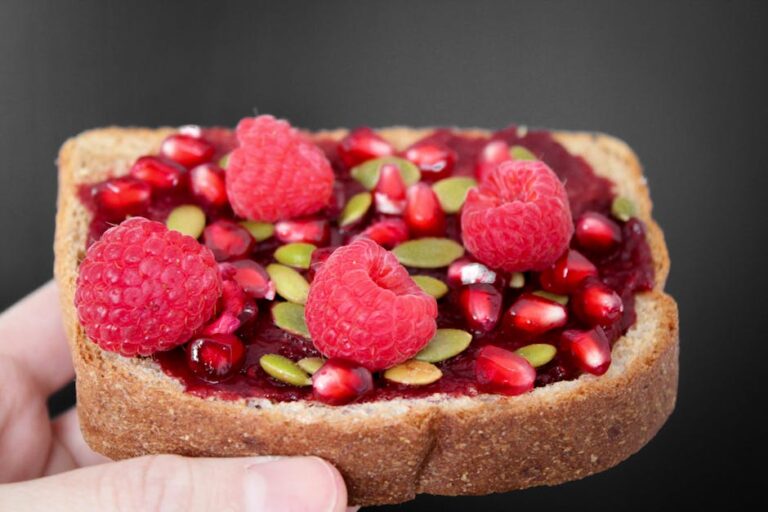 Close-up of a delicious multigrain toast topped with raspberries, pomegranate seeds, and pumpkin seeds.
