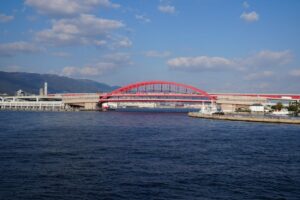 Bright red bridge over Kobe port under a clear autumn sky, showcasing modern architecture.