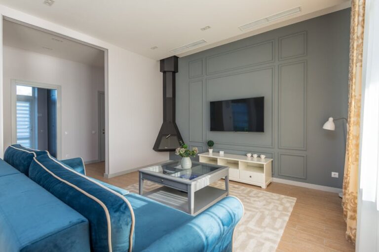 A stylish living room featuring a blue couch, wall-mounted TV, and elegant decor.