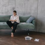 Woman sitting on a couch in an industrial-style living room, engaged in reading or working.