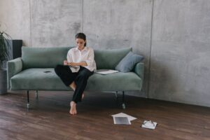 Woman sitting on a couch in an industrial-style living room, engaged in reading or working.