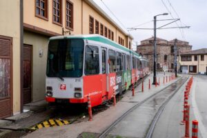 A red tram parked along a street near a historical building in an urban area.