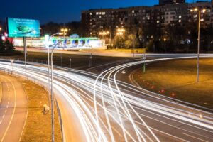 A dynamic city night scene showcasing light trails on roads with illuminated buildings in the background.