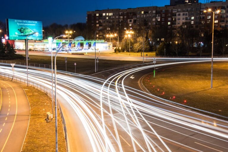 A dynamic city night scene showcasing light trails on roads with illuminated buildings in the background.