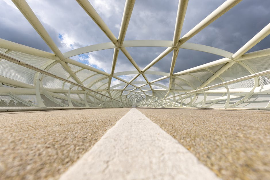 Low angle view of a modern bridge with a geometric metal arch against a cloudy sky.