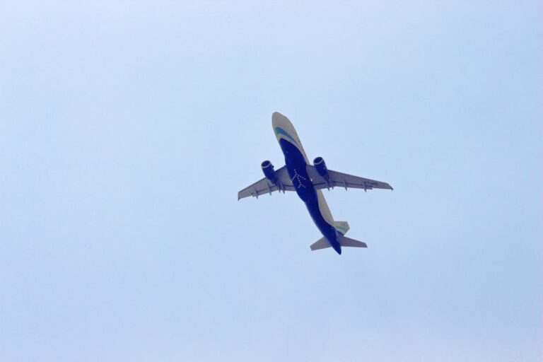 A commercial airplane captured in mid-flight against a clear blue sky, viewed from below.