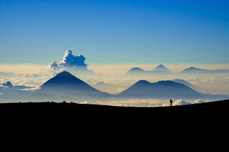 Silhouette of a hiker walking with distant volcanoes and a sea of clouds in Guatemala.