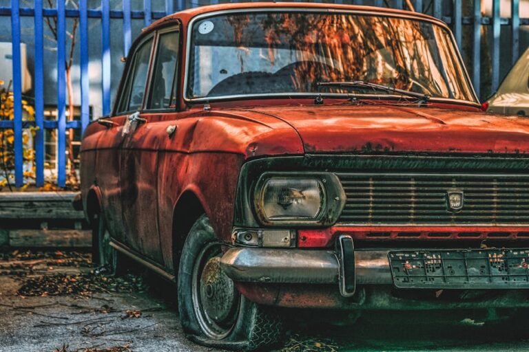 An atmospheric image of a rust-covered vintage car parked in an urban outdoor space.