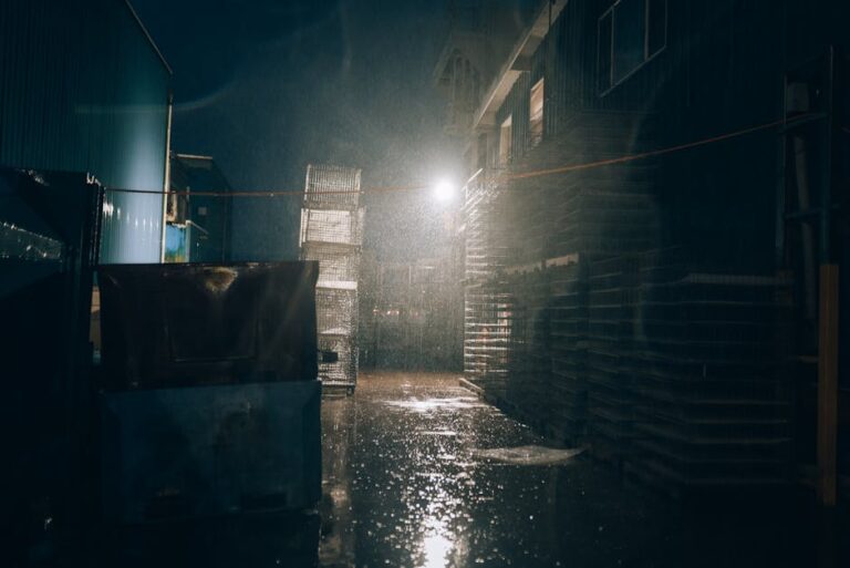 Mysterious urban alley at night during heavy rain, with dim lighting creating a moody atmosphere.
