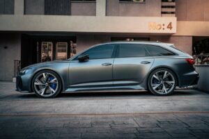 Side view of a sleek metallic car parked in front of an urban residential building with a sign 'No: 4'.
