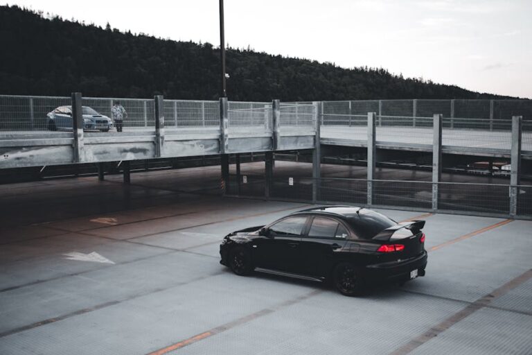 A black car parked alone in a spacious parking lot during twilight, creating a moody atmosphere.