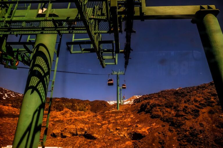 Green steel cable cars traverse a rocky mountain landscape under a clear blue sky.