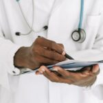 Professional doctor writing on a clipboard with a stethoscope in a medical office.