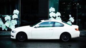 A stylish white coupe car parked outdoors with floral window display background.