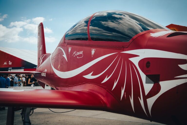 Dynamic close-up of a red aerobatic aircraft displayed at an outdoor airshow, featuring sleek design.