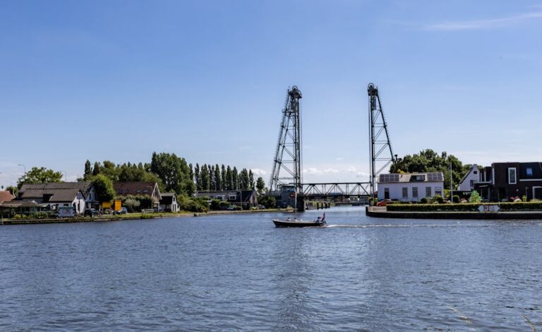 A serene river with a drawbridge, boat, and picturesque houses under a clear sky.
