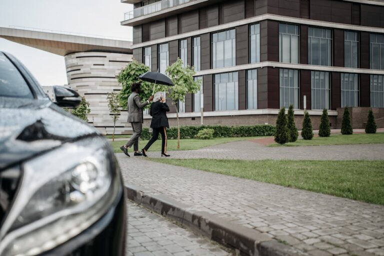 Two business professionals walking with an umbrella outside a modern building.