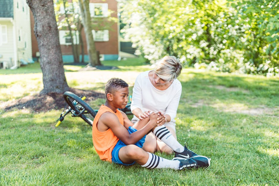 A woman comforts an injured child beside a bicycle in a sunny park setting.