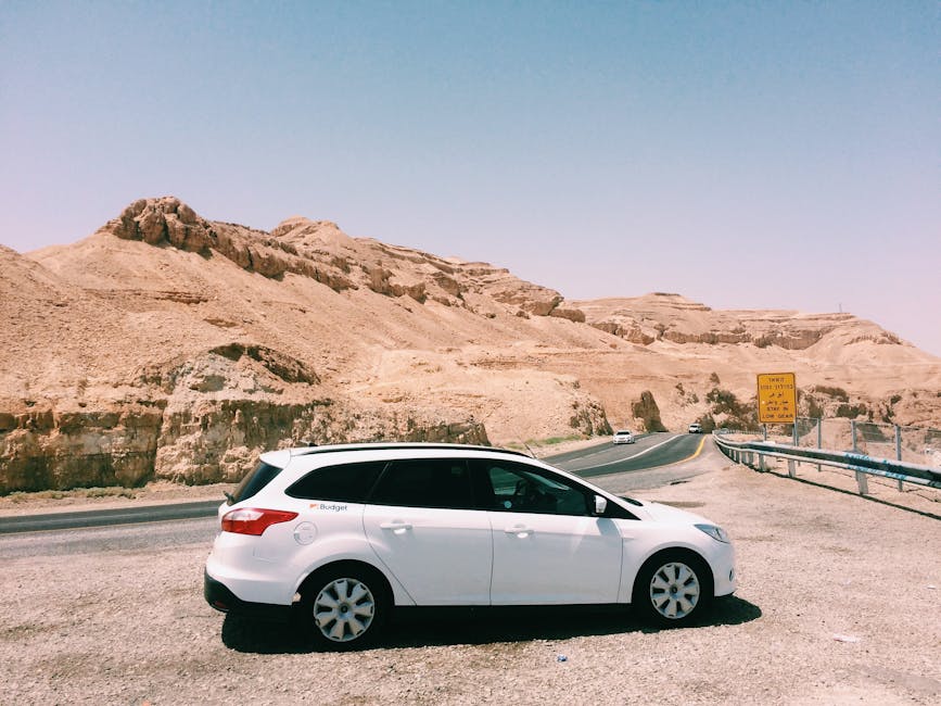 White car parked by a desert highway with scenic desert mountains and clear blue sky in the background.