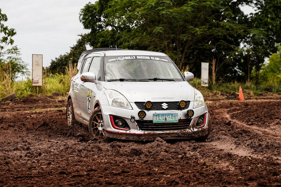 A white rally car in action on a muddy course, captured outdoors during daytime.