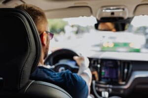 Close-up of a man driving a modern vehicle from behind with a blurred urban background.