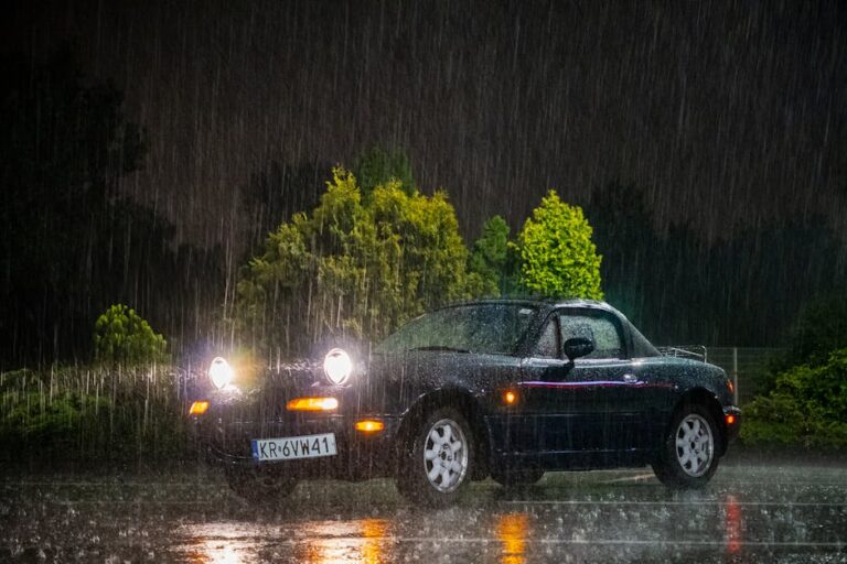 A Mazda Miata drives through heavy rain at night, highlighting vehicle's resilience and enduring style.