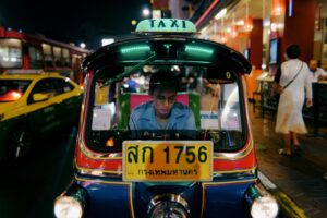 Tuk-tuk taxi driver focused while navigating through Bangkok's lively city streets at night.