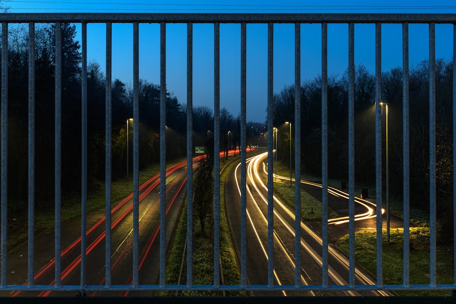 Long exposure of a highway's light trails through a guardrail at dusk in Craigavon, Northern Ireland.