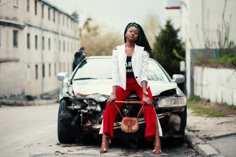 Fashionable woman poses confidently on a damaged car in an urban environment.