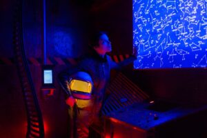 Astronaut in space suit analyzing a futuristic star map in a dimly lit chamber.