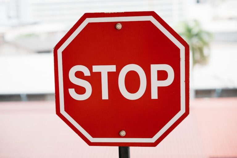 A red stop sign with bold white text in an urban setting, signaling caution.