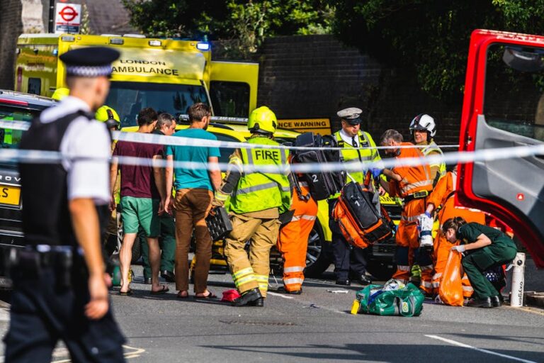 Emergency responders assisting at a street accident in London with visible metro station sign.