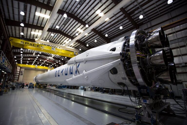 A SpaceX Falcon rocket displayed in a spacious hangar under bright industrial lights.
