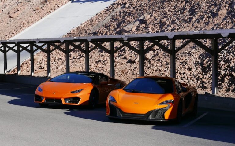 Two orange luxury sports cars parked under a wooden structure in Boulder City, Nevada.
